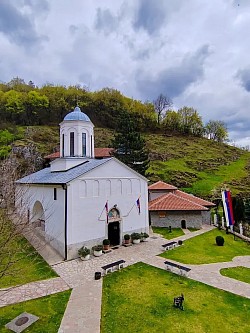 Манастир Свете Тројице Пљевља - Панорамски поглед на спољашњу архитектуру манастира Свете Тројице у Пљевљима са високим каменим зидовима и препознатљивим звоником који се уздиже изнад манастирске порте  Главни храм манастира Свете Тројице Пљевља посматран са улазне капије при чему се види складна градња од камена и специфичан кровни покривач типичан за средњовековне српске светиње